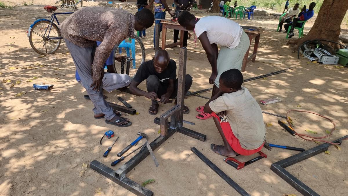 Designers gather around metal and wood pieces and tools while outside on a sunny day.